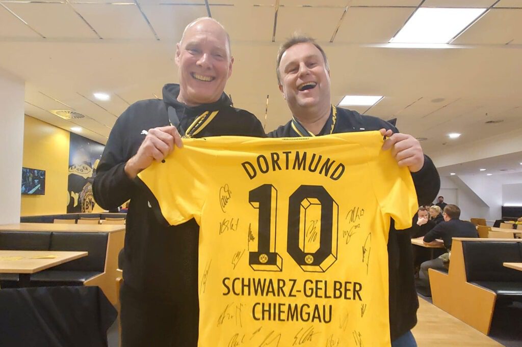 Zwei Männer halten ein signiertes gelbes Dortmund-Trikot mit der Nummer 10 und der Aufschrift Schwarz-Gelber Chiemgau.