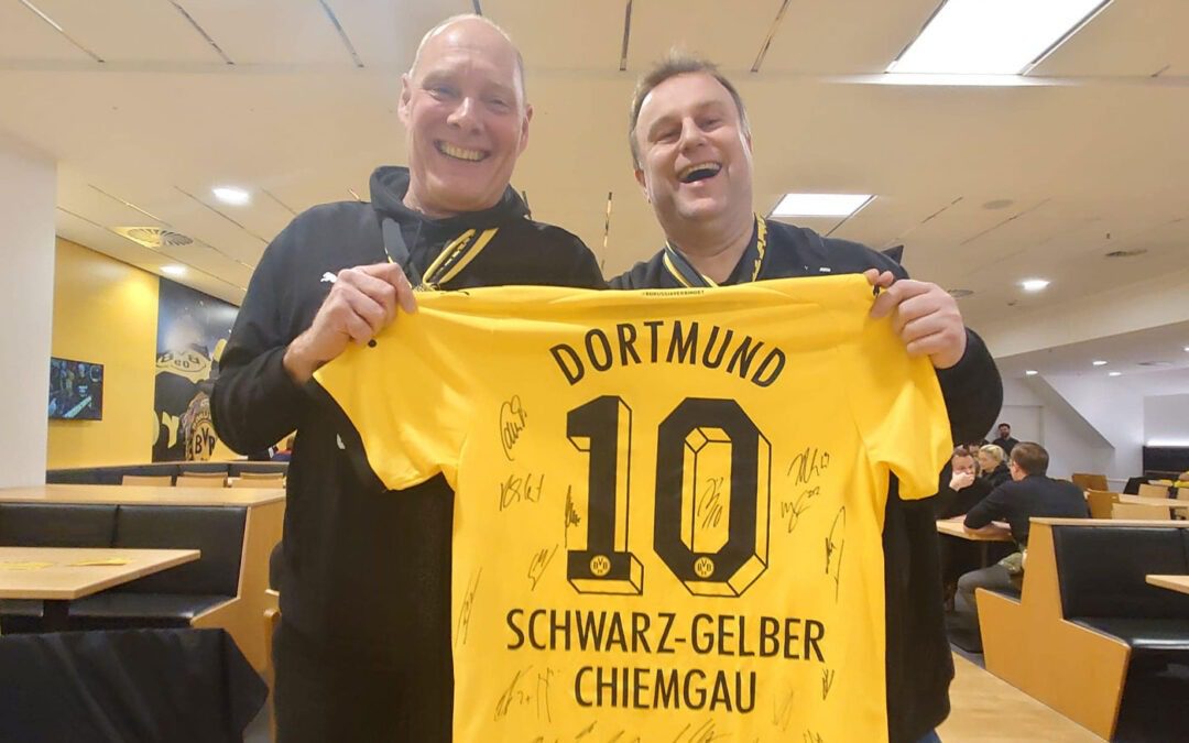 Zwei Männer halten ein signiertes gelbes Dortmund-Trikot mit der Nummer 10 und der Aufschrift Schwarz-Gelber Chiemgau.