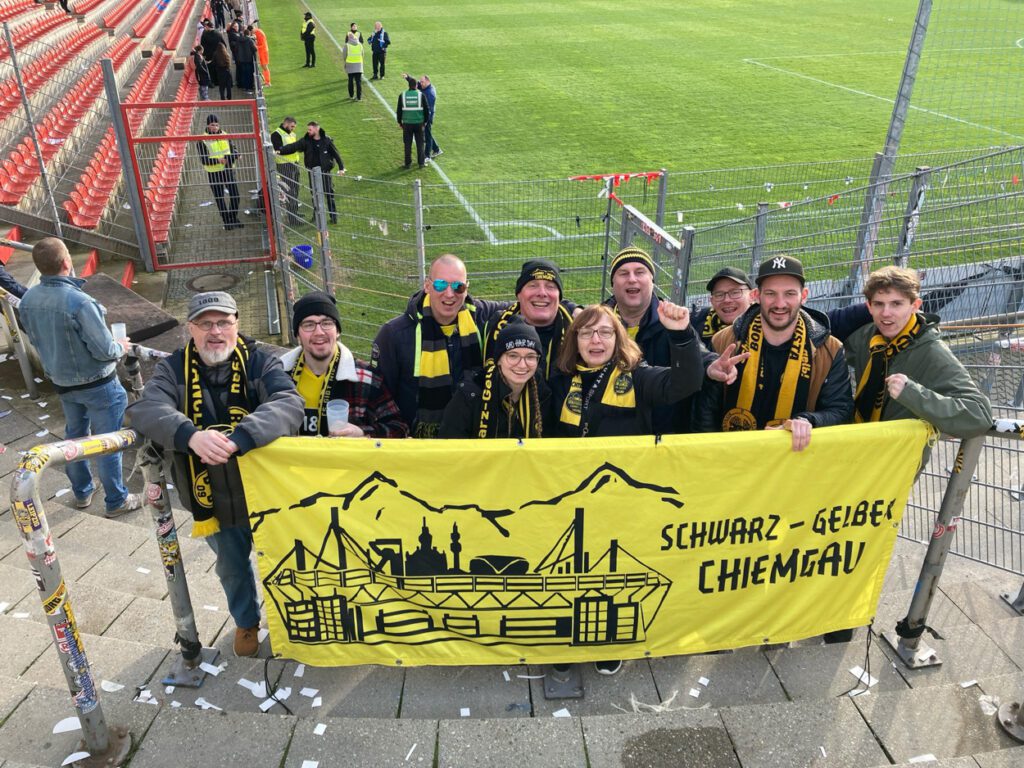 Rund zehn Mitglieder stehen auf der Tribüne hinter dem gelben Banner des Schwarz-Gelben Chiemgau.