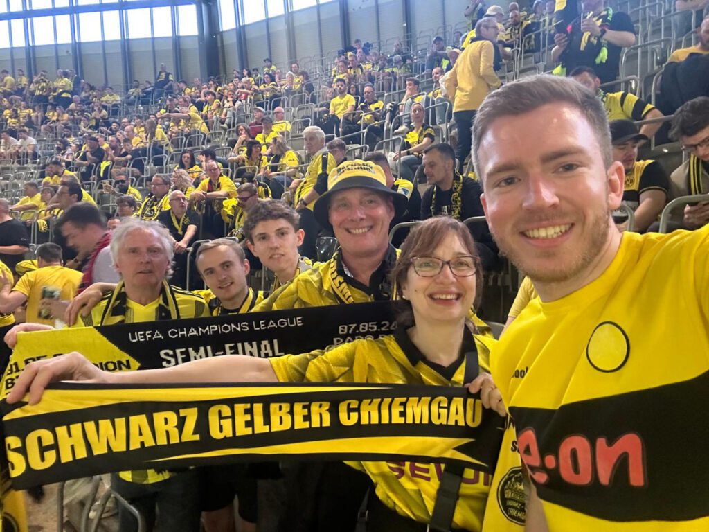 Mitglieder halten auf der vollen Tribüne einen Schal des Schwarz-Gelben Chiemgau und einen Halbfinal-Schal.