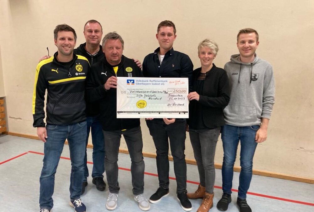 Sechs Personen, teils in BVB-Jacken, halten in einer Sporthalle einen großen Spendenscheck.