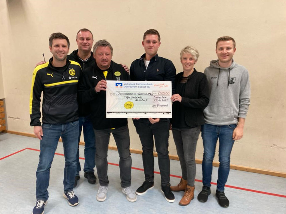 Sechs Personen, teils in BVB-Jacken, halten in einer Sporthalle einen großen Spendenscheck.