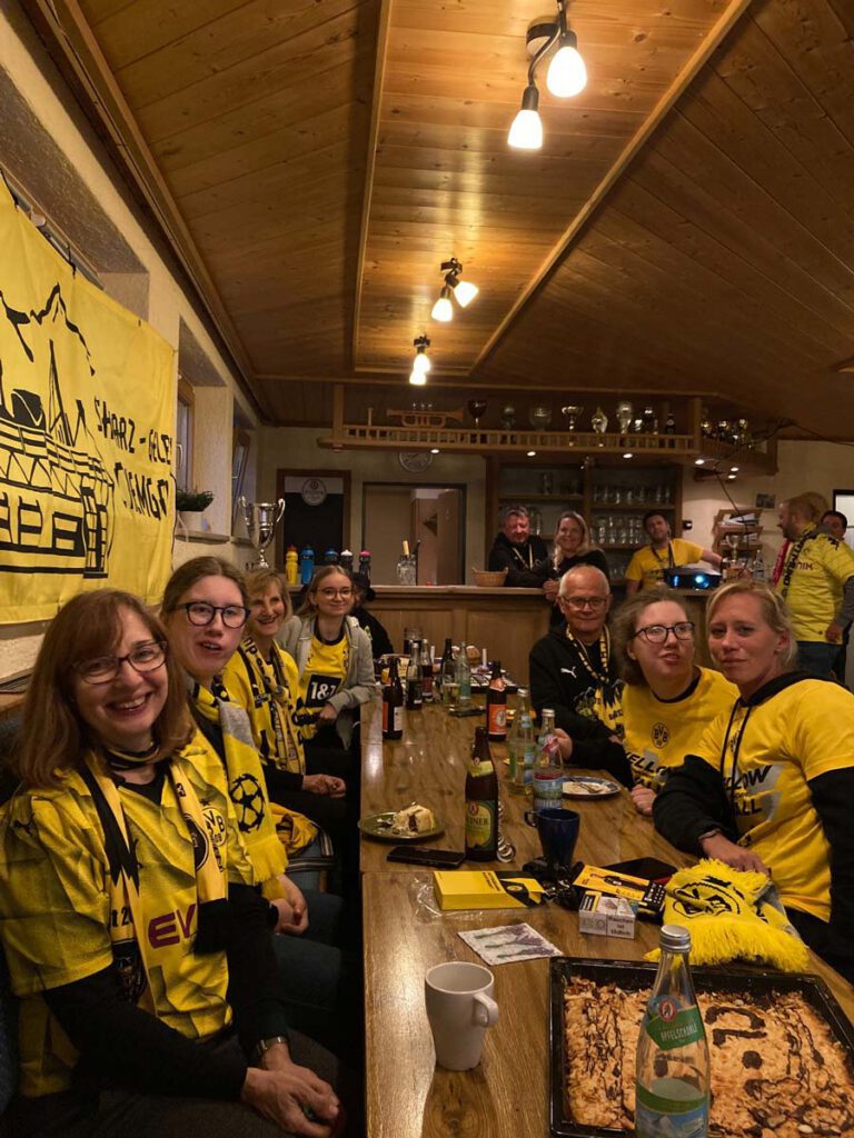 Mitglieder in BVB-Trikots sitzen an einer langen Tafel in einer holzvertäfelten Gaststube mit BVB-Deko.