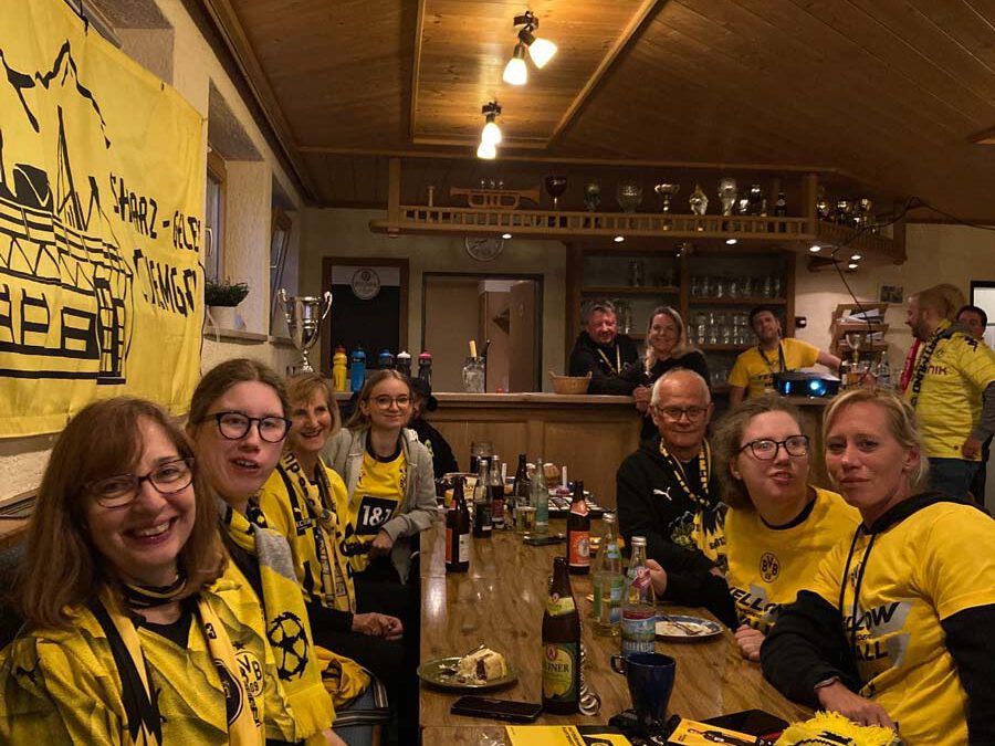 Mitglieder in BVB-Trikots sitzen an einer langen Tafel in einer holzvertäfelten Gaststube mit BVB-Deko.