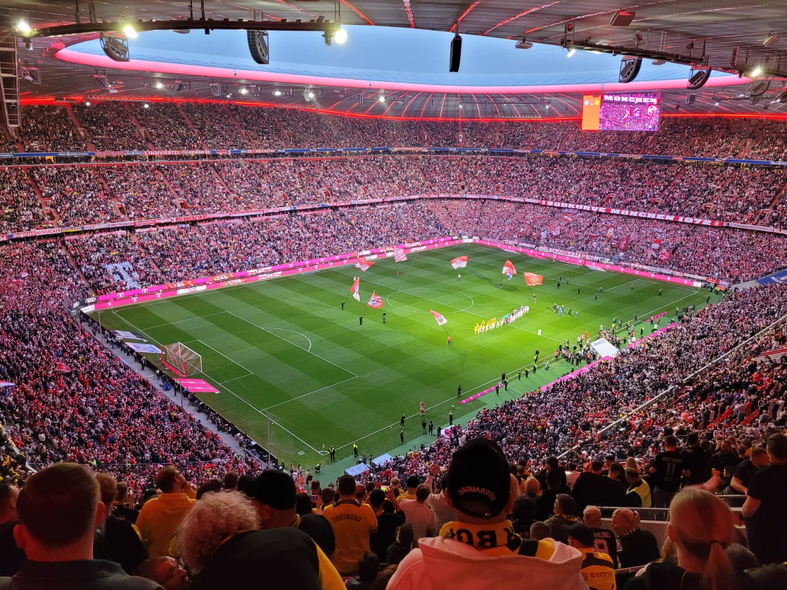 Blick von oben in die volle Allianz Arena mit roten Rängen und leuchtendem Dachrand, unten das Spielfeld.