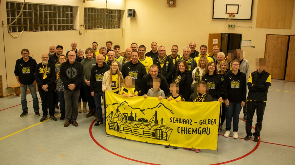 Rund vierzig Mitglieder stehen in einer Turnhalle in Reihen, vorne halten einige das gelbe Fanclub-Banner.
