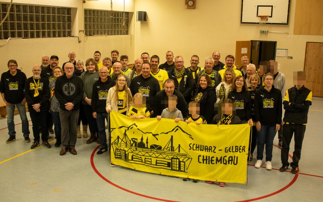 Rund vierzig Mitglieder stehen in einer Turnhalle in Reihen, vorne halten einige das gelbe Fanclub-Banner.