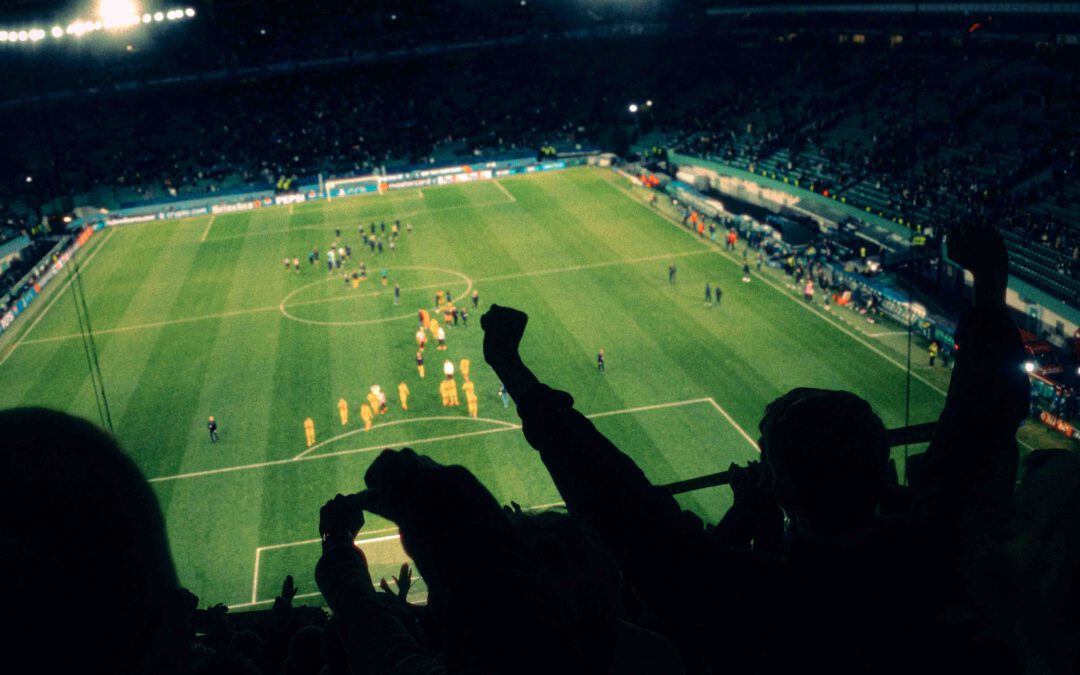 Fans recken die Fäuste in die Luft, auf dem Rasen unter Flutlicht jubelt die Mannschaft in Gelb.