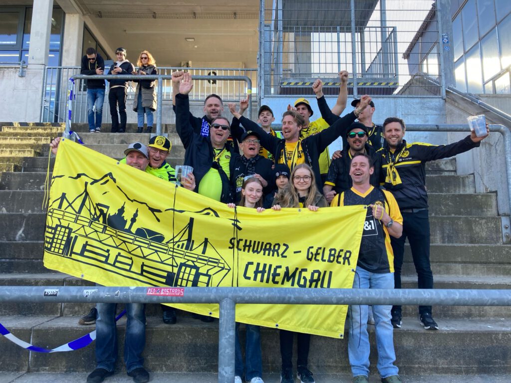 Rund zehn Mitglieder stehen auf Tribünenstufen hinter dem gelben Banner des Schwarz-Gelben Chiemgau.