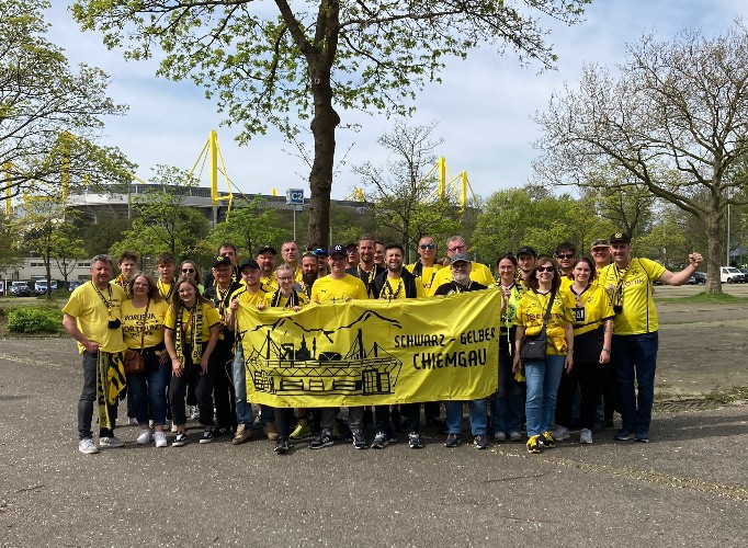 Rund 20 Mitglieder in gelben Shirts stehen unter Bäumen hinter dem Fanclub-Banner, im Hintergrund gelbe Stadionpylonen.