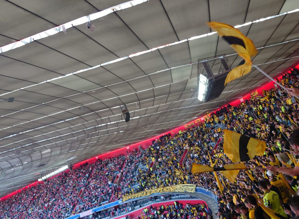 Schwarz-gelbe Fahnen im Gästeblock unter dem weißen Dach der Allianz Arena, ringsum rote Ränge.