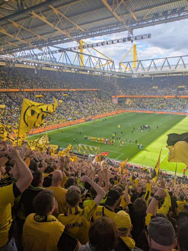 Volle Tribüne mit schwarz-gelben Fahnen unter dem gelben Stahldach, Blick auf das Spielfeld.