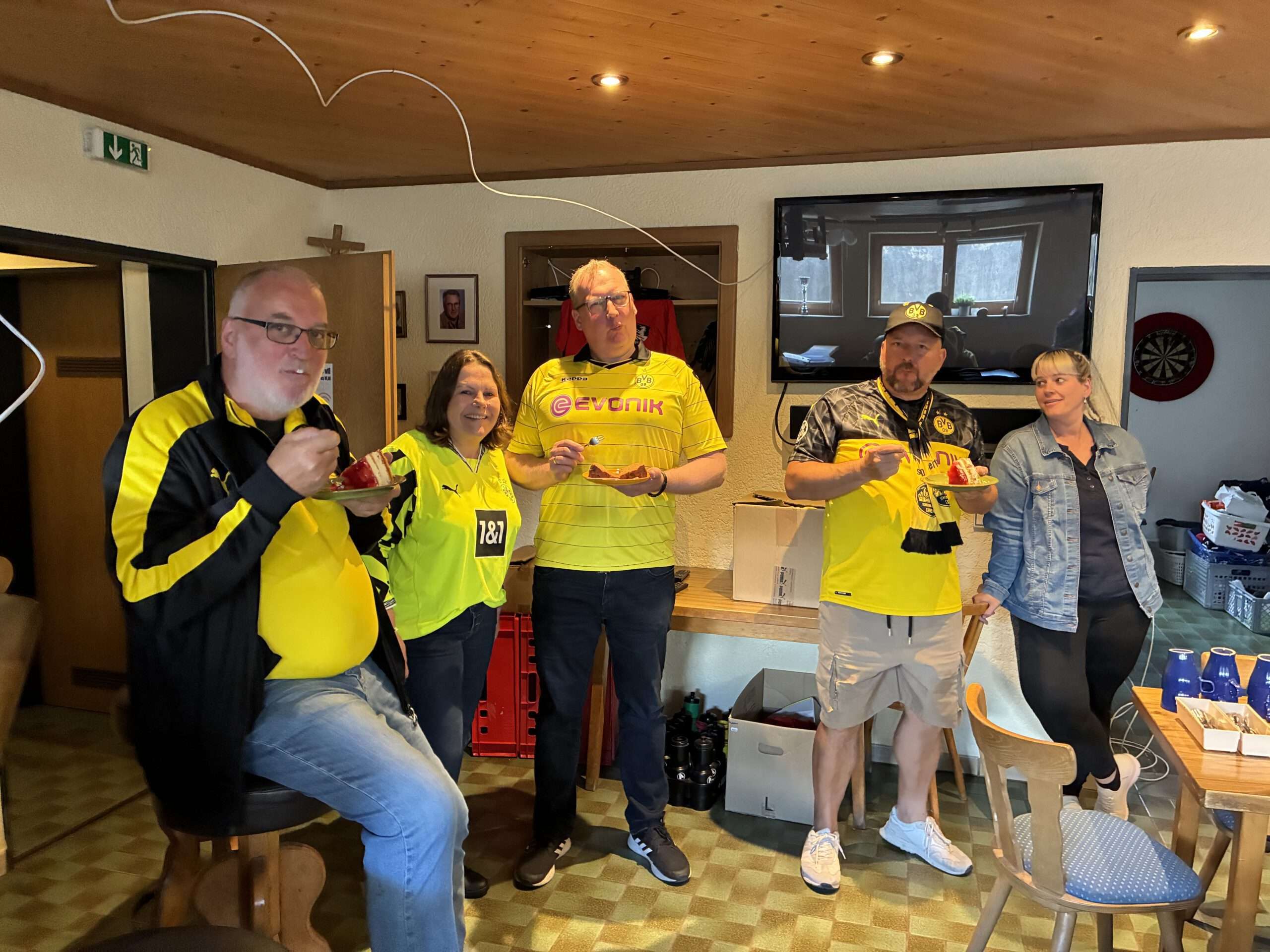 Sommerfest 2025 Vier Mitglieder in BVB-Trikots stehen mit Getränken in der Hand in einem Gastraum mit Fernseher.