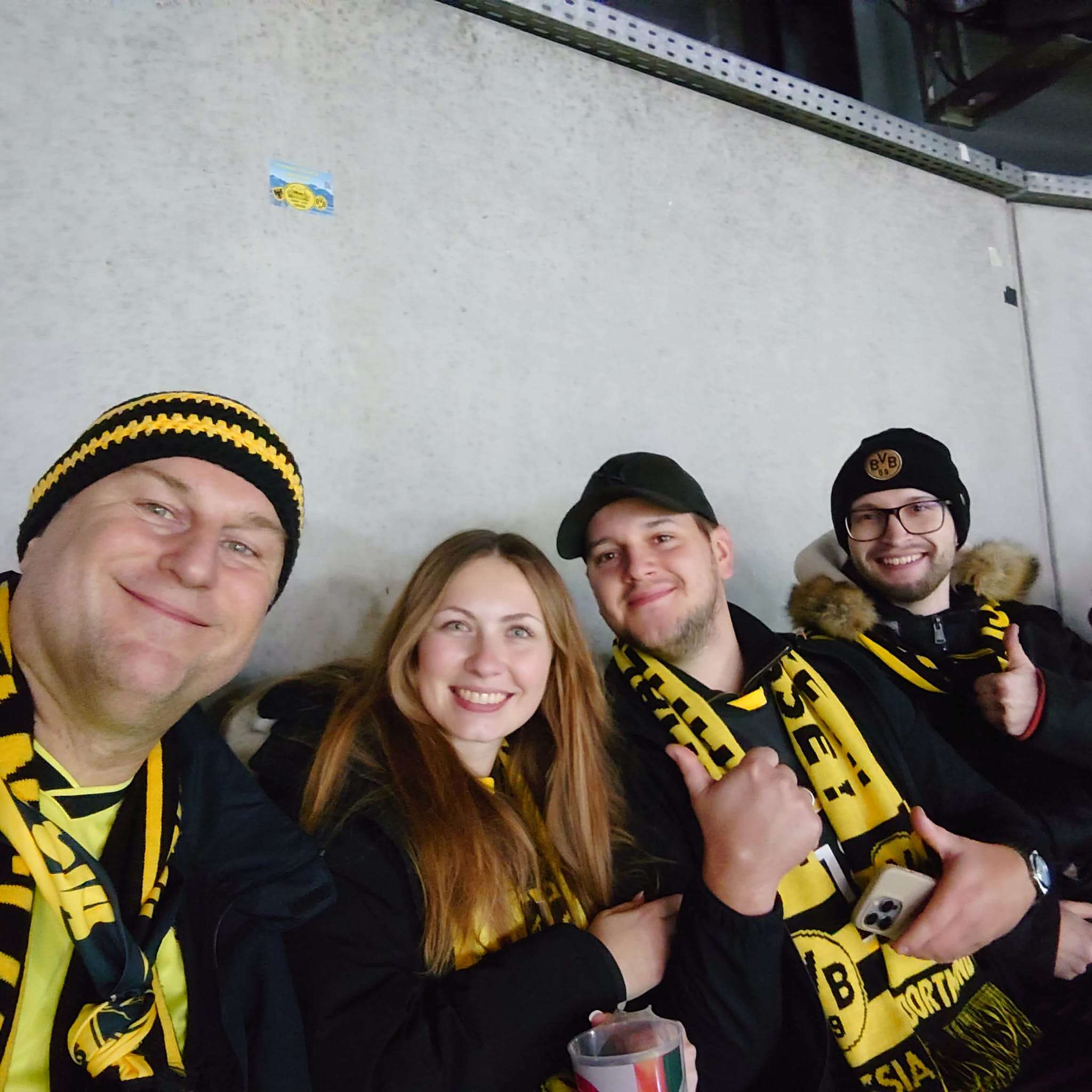 Vier Mitglieder mit BVB-Mützen und Schals machen ein Selfie vor einer grauen Betonwand.
