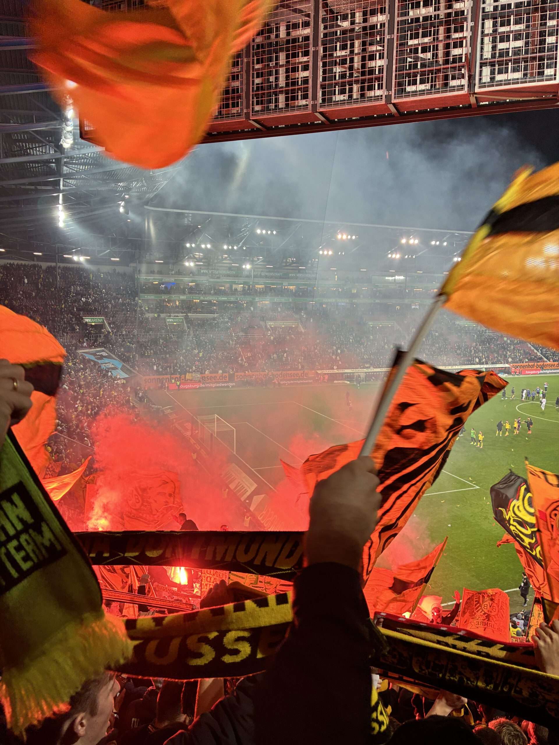 Rot leuchtende Bengalos, Rauch und schwenkende Fahnen im dunklen Gästeblock.