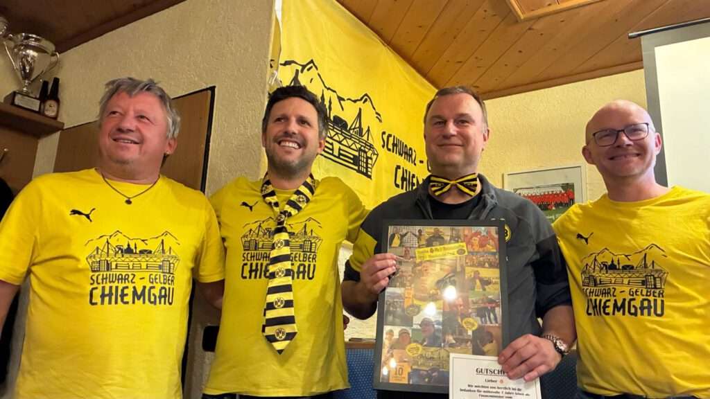 Vier Männer in Fanclub-Shirts stehen nebeneinander, einer hält ein gerahmtes Geschenk.