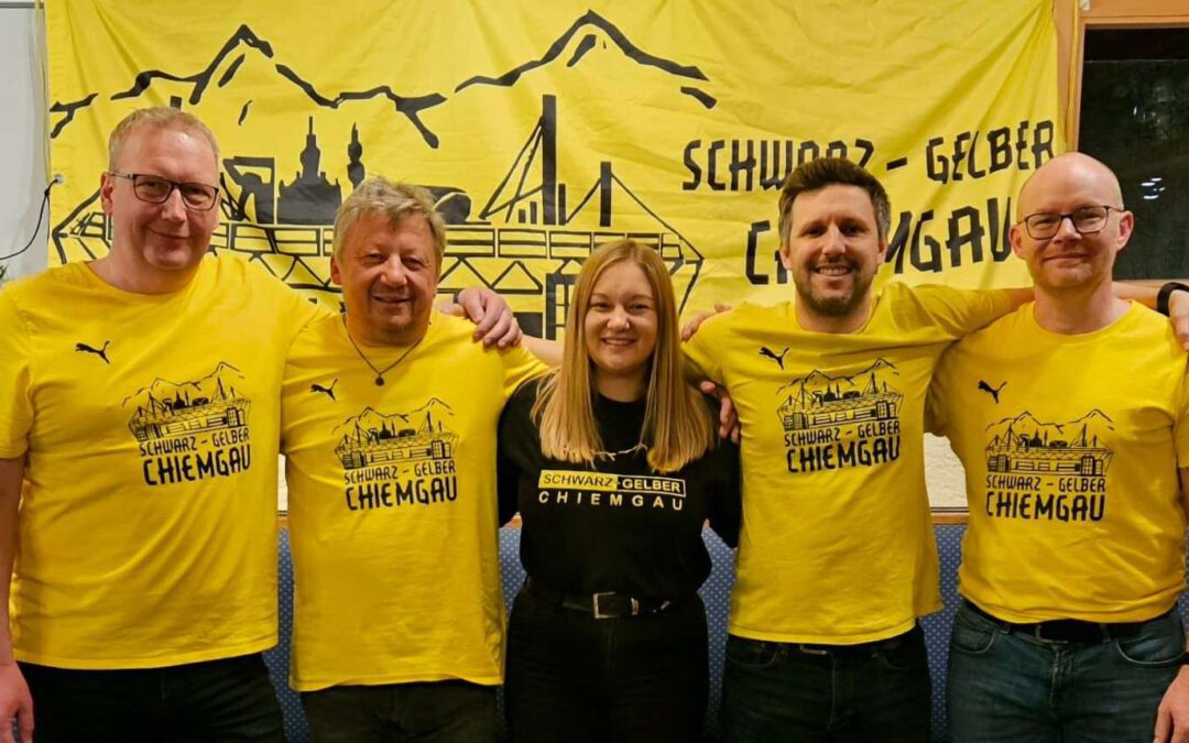 Fünf Personen in gelben Fanclub-Shirts stehen vor dem großen Banner des Schwarz-Gelben Chiemgau.
