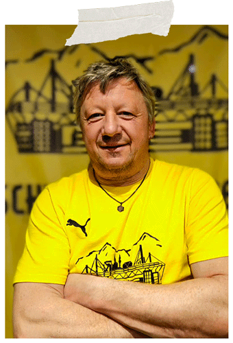 Angeheftetes Foto: Mann mit verschränkten Armen im gelben Fanclub-T-Shirt vor dem gelben Fanclub-Banner.