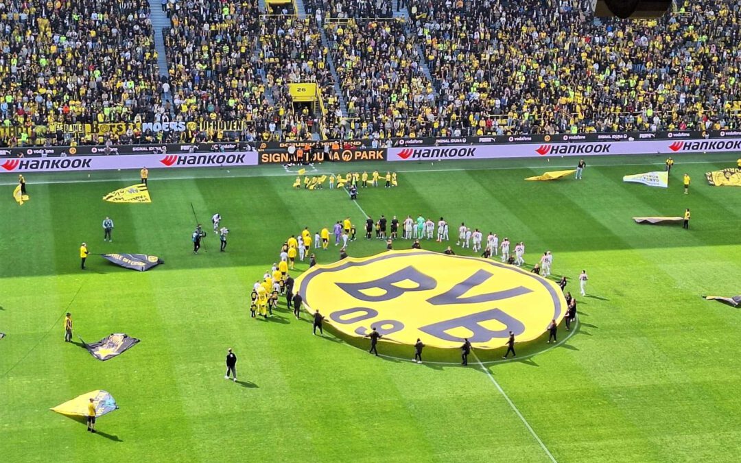 Großes BVB-Logo als Fahne im Mittelkreis, ringsum Fahnenträger auf dem Rasen und volle Ränge.